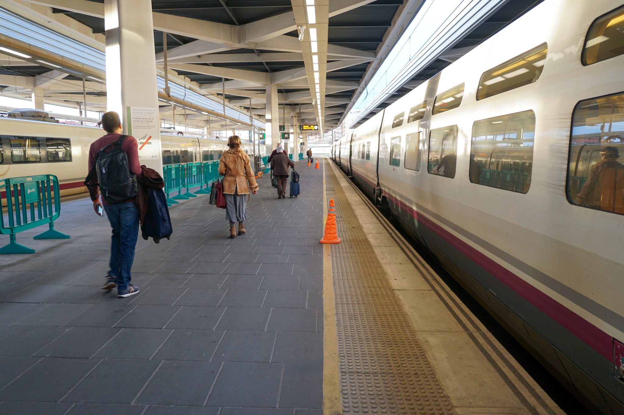 A train station platform with people walking alongside a stationary passenger train. Several individ