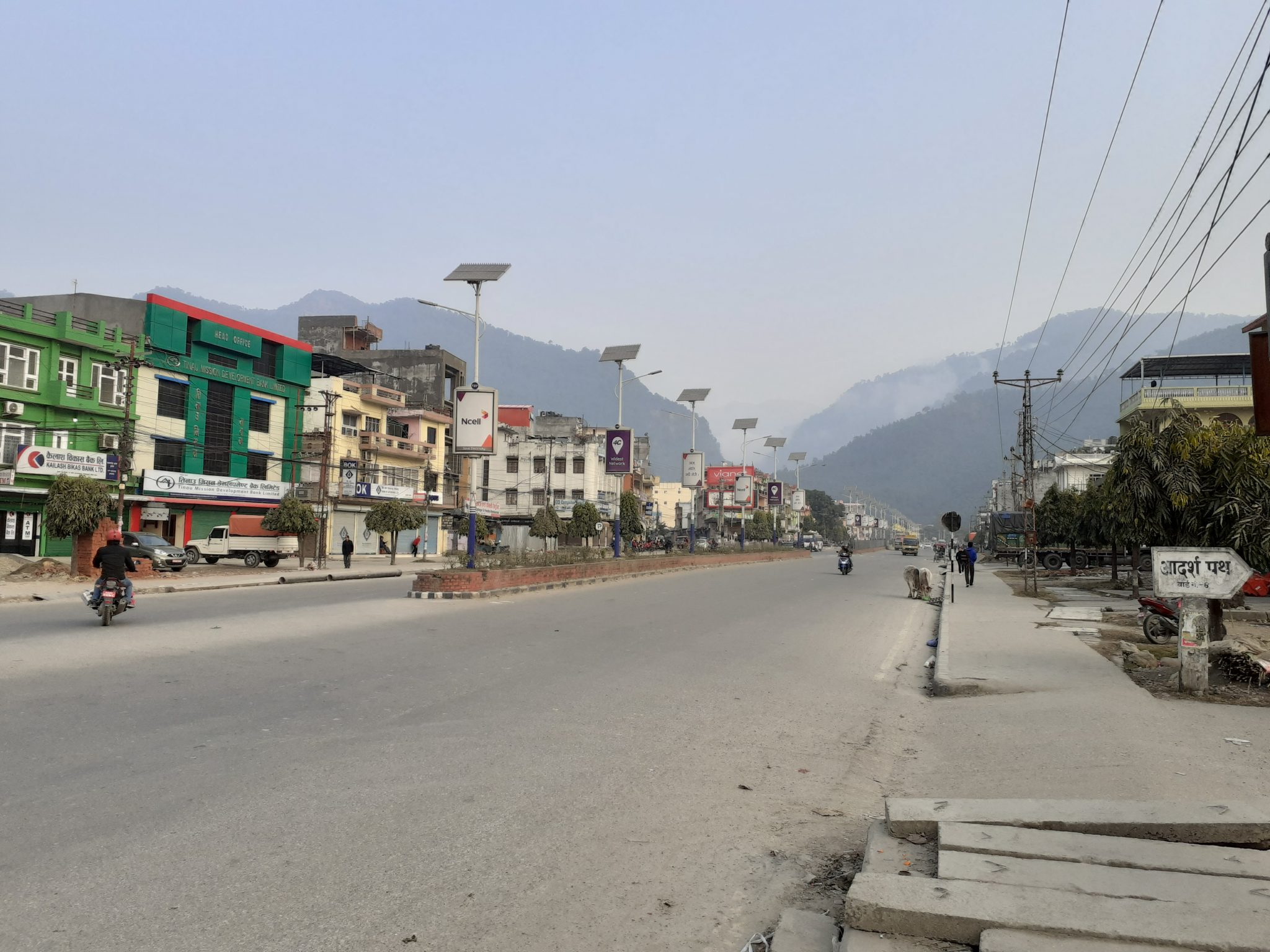A quiet street scene in a mountainous area, featuring a wide road flanked by shops and buildings of 