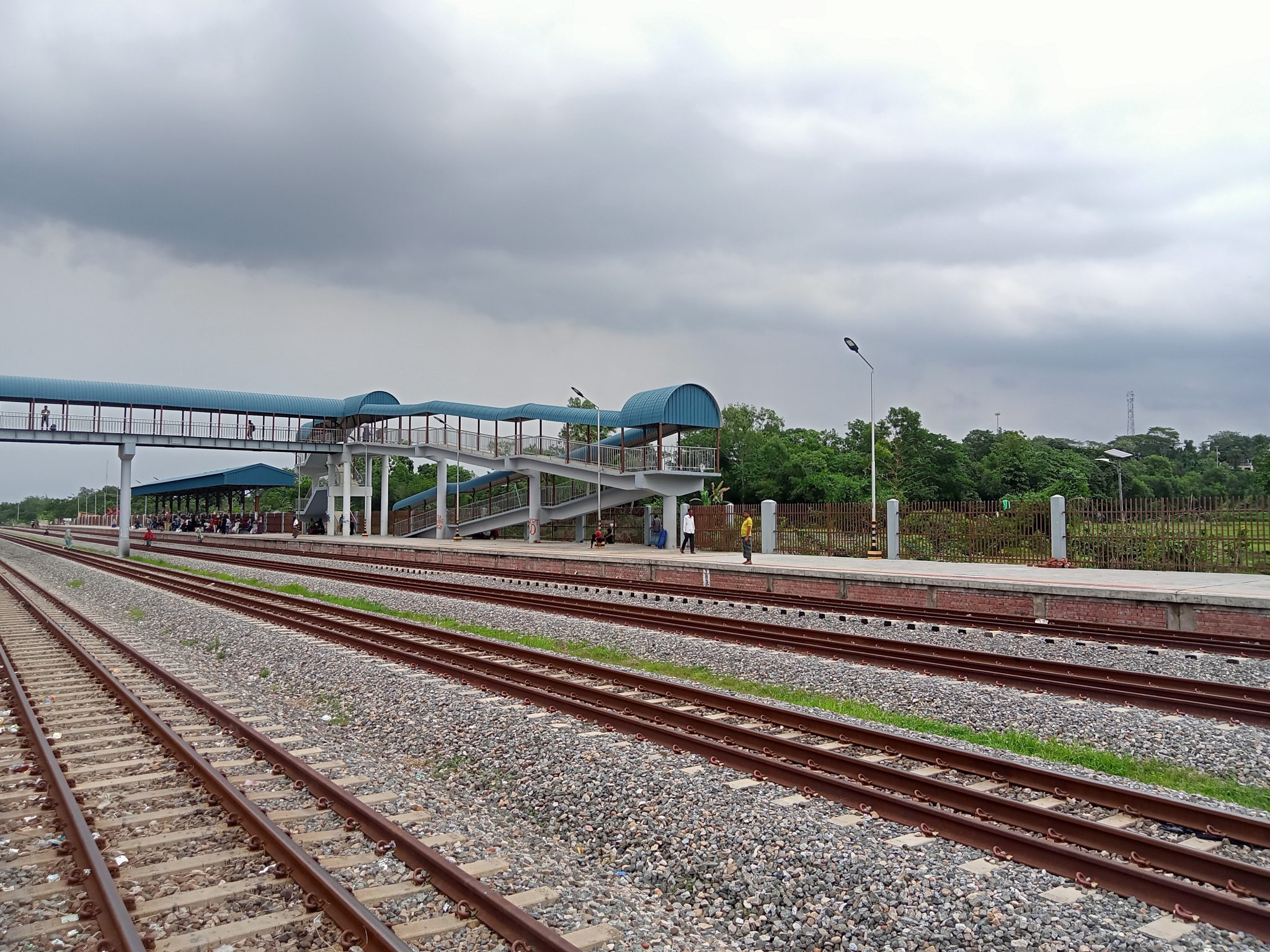 The image shows a railway station platform with multiple train tracks in the foreground. A modern pe