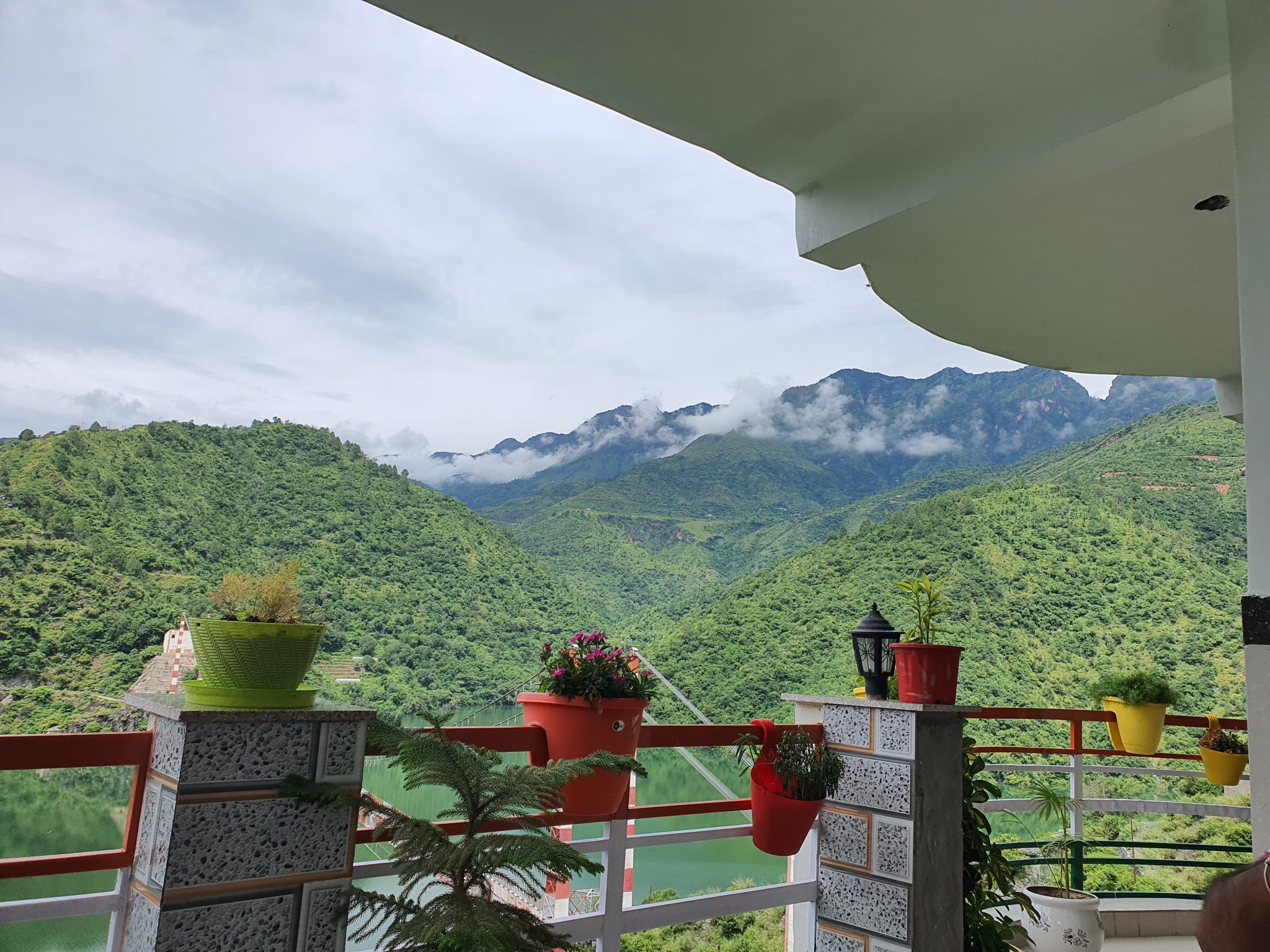 Vibrant greenery and a mountain range beneath clear skies, View from a balcony with colourful flower