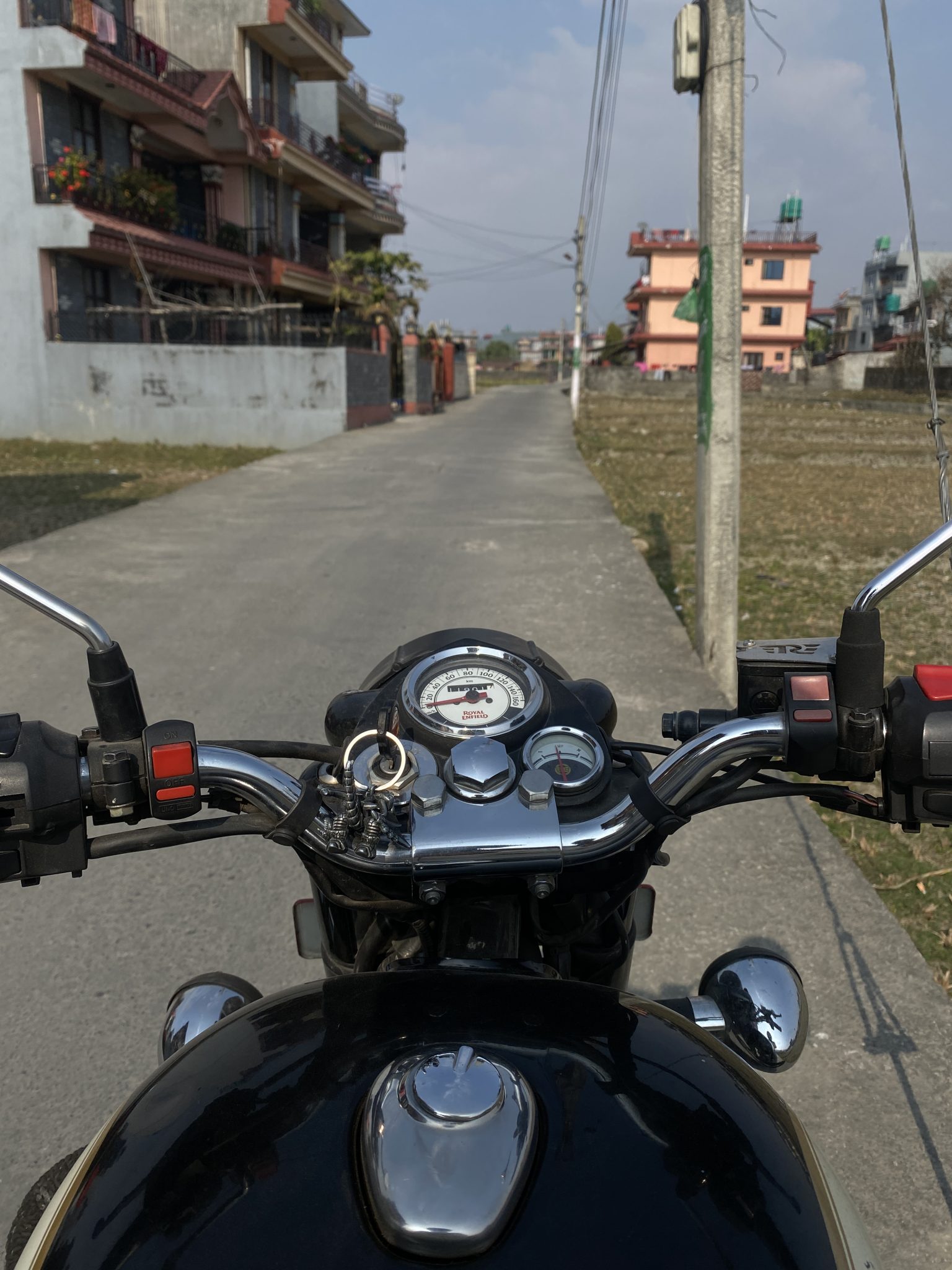 View from a motorcycle on a quiet street with residential buildings. The sun casts a warm glow, crea