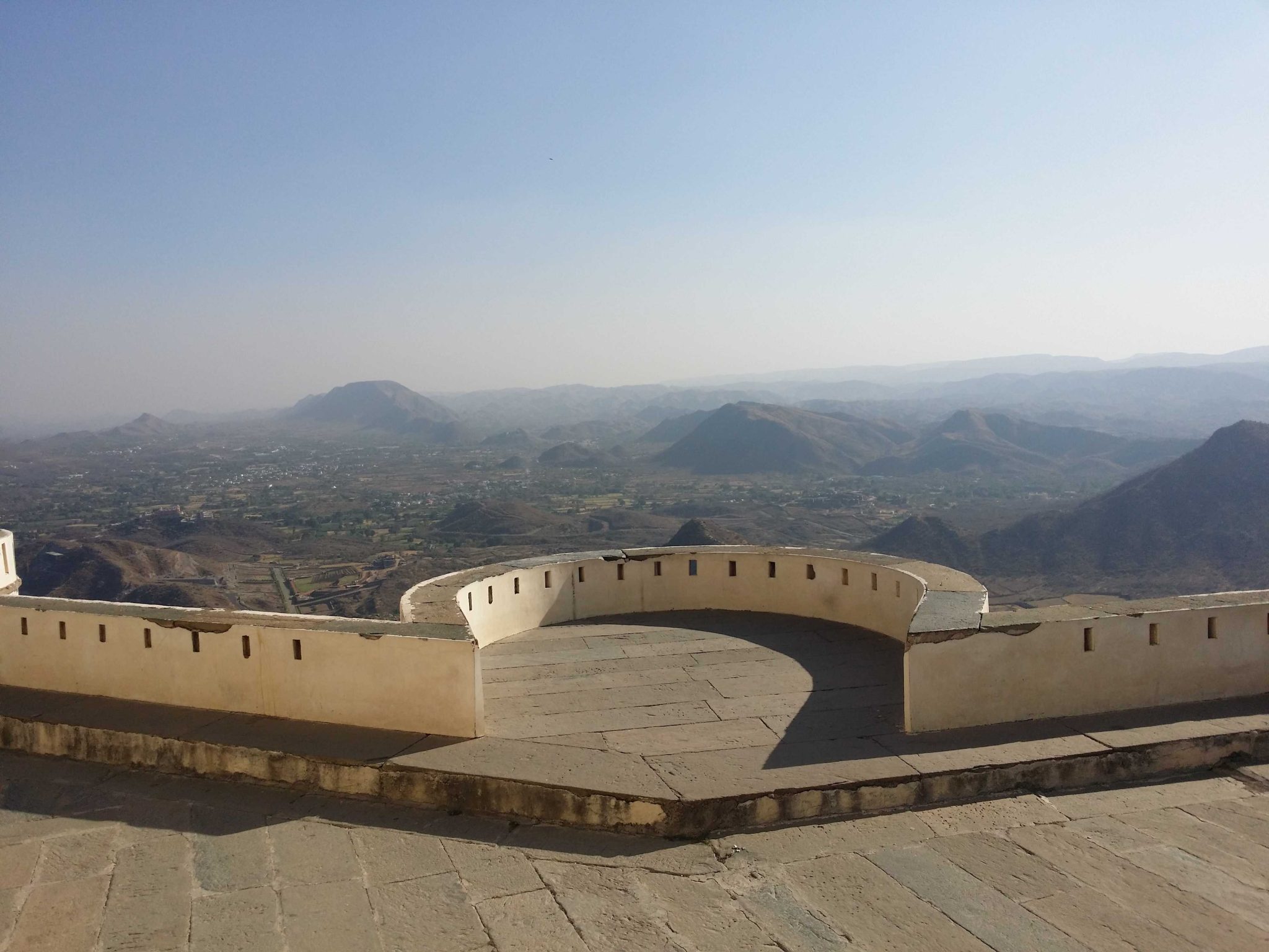 A scenic view from a fort balcony overlooking a vast landscape of rolling hills and valleys under a