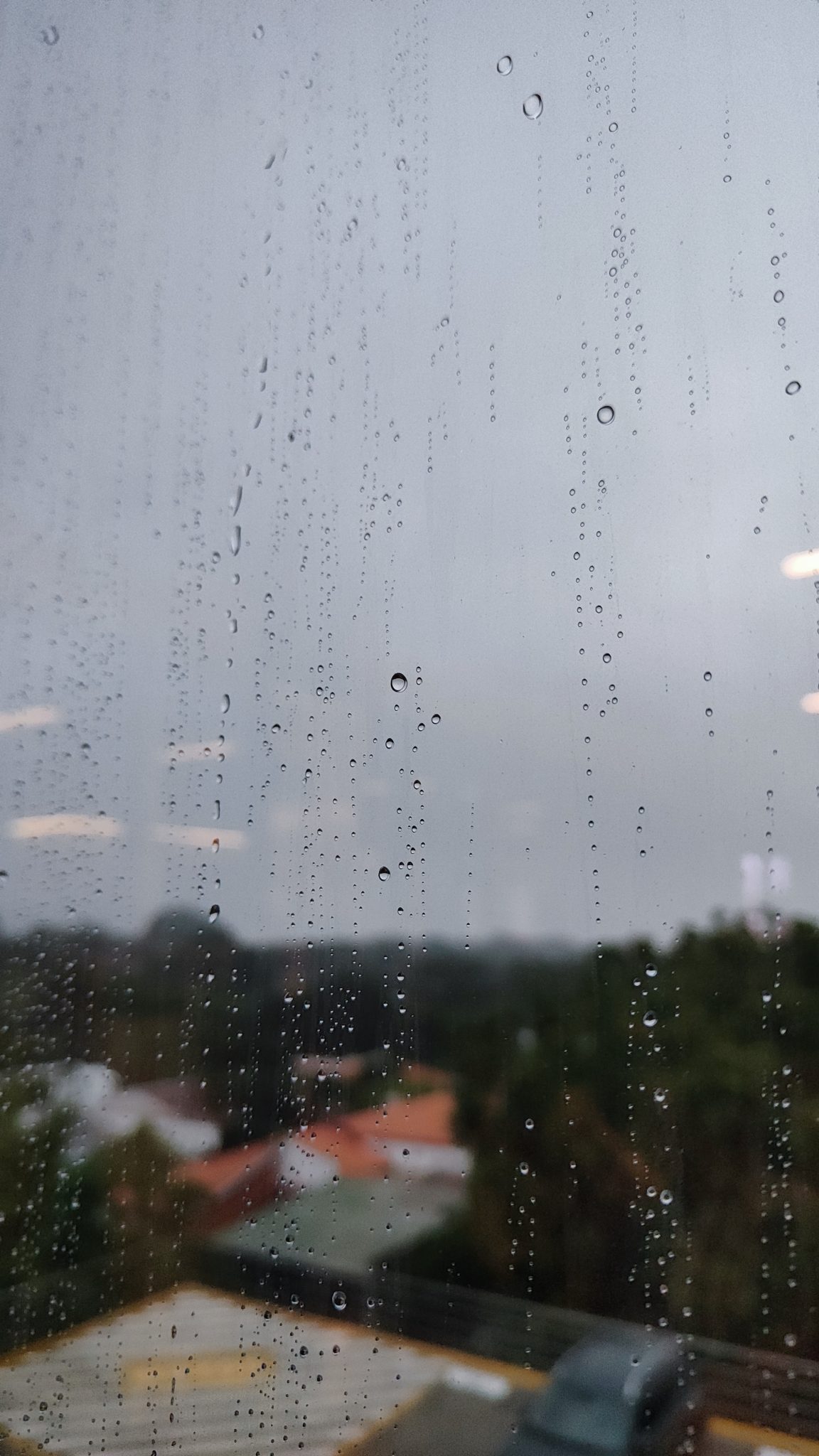 Raindrops on a window with a blurred view of buildings and trees outside, depicting a rainy and over