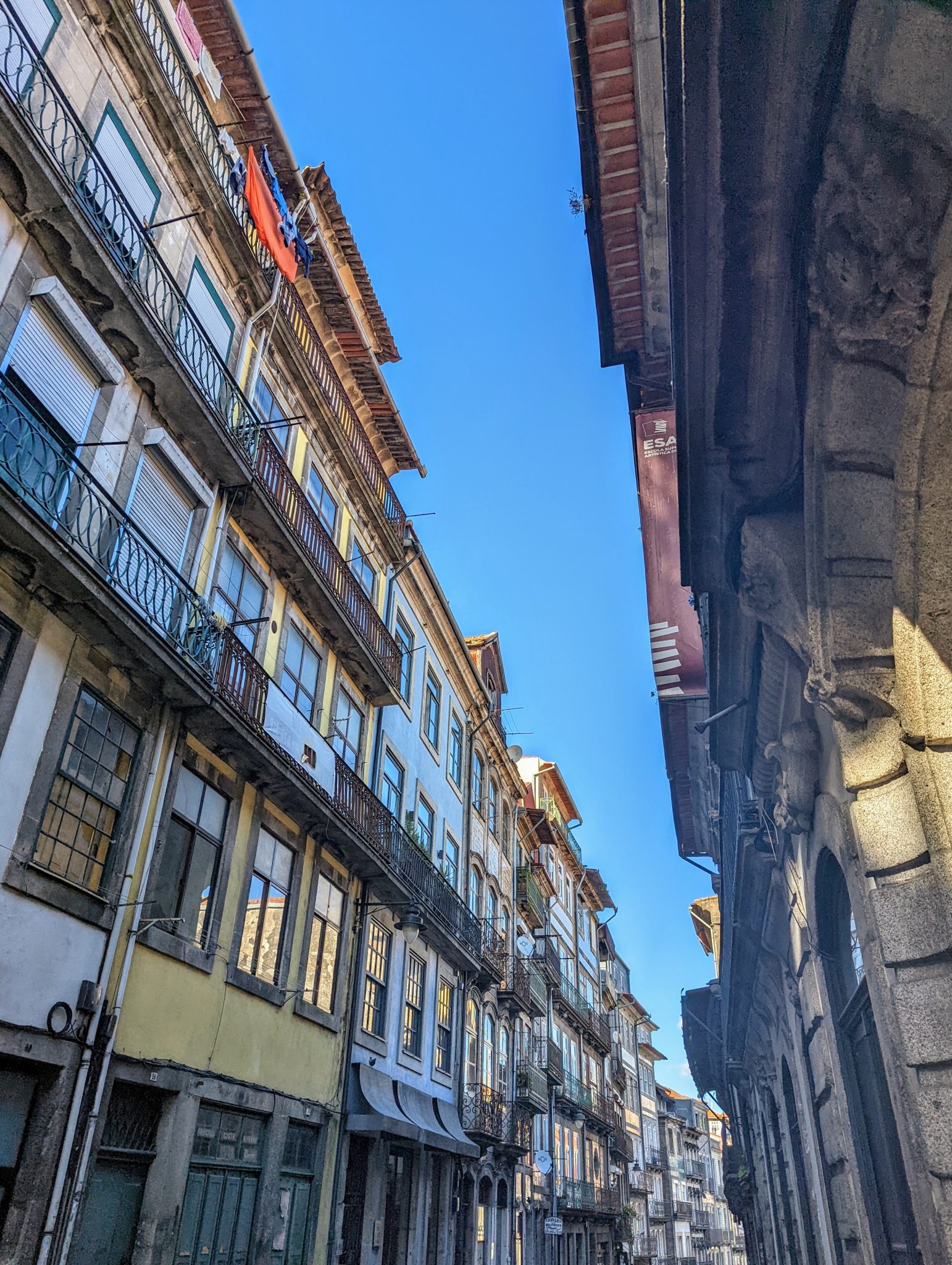 A narrow street lined with tall, historical buildings featuring traditional balconies and varied arc