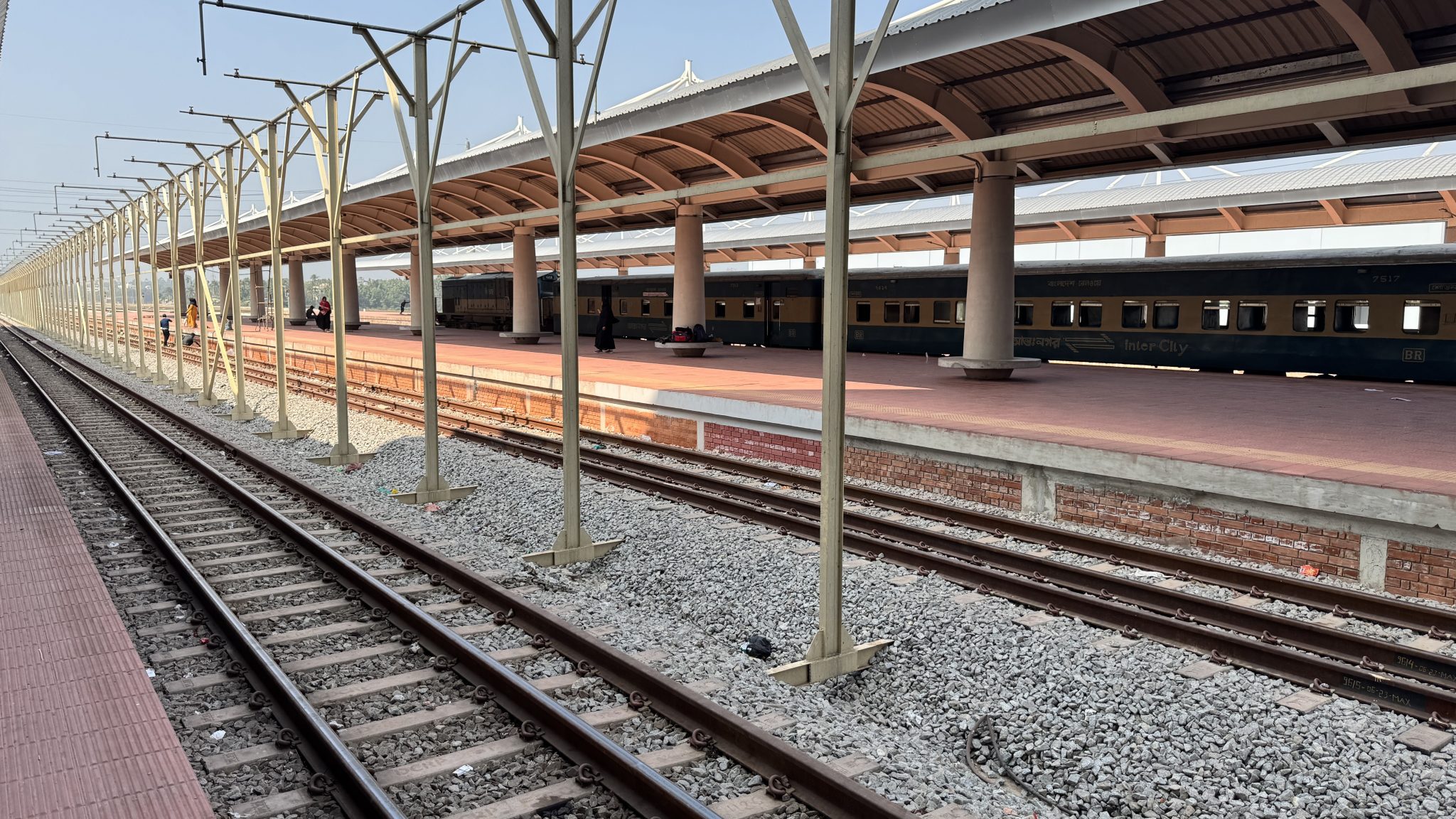 A train station platform with metal supports and a roof is visible, featuring several train carriage