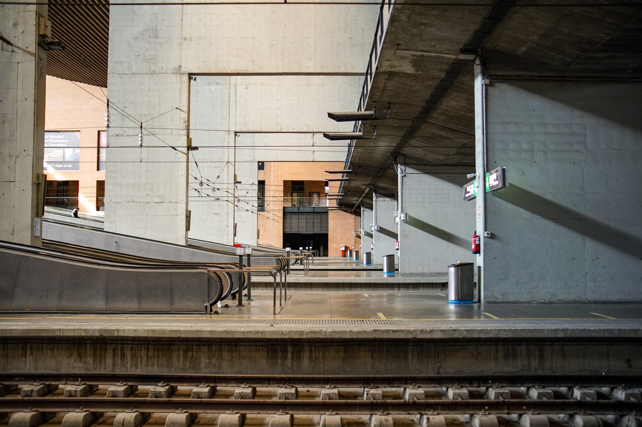 A train station platform with two sets of tracks in the foreground. There are escalators and stairs